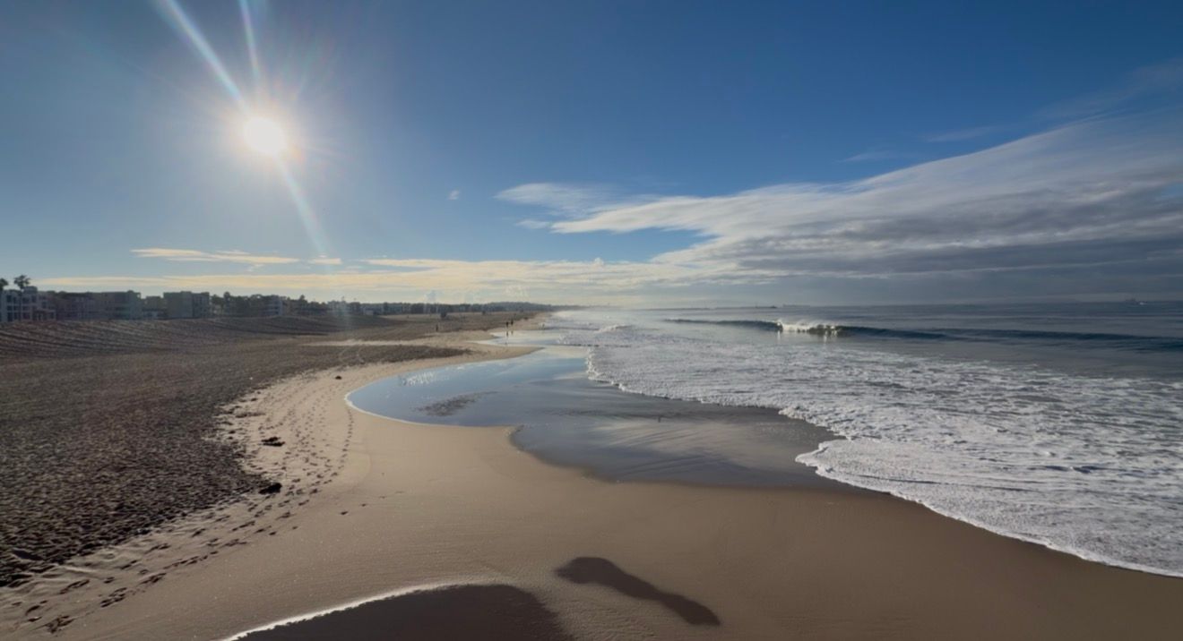 Hand holding a handwritten note reading New day, new strength, new thoughts, new possibilities against a sunny beach and ocean waves.
