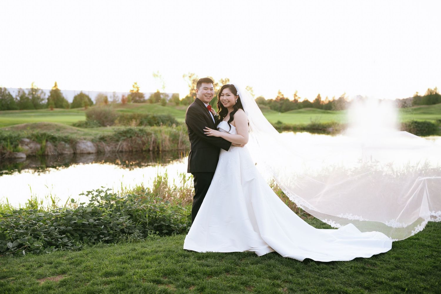 Jennifer and Riley embracing by the pond at sunset during their Riverway Clubhouse wedding in Burnaby