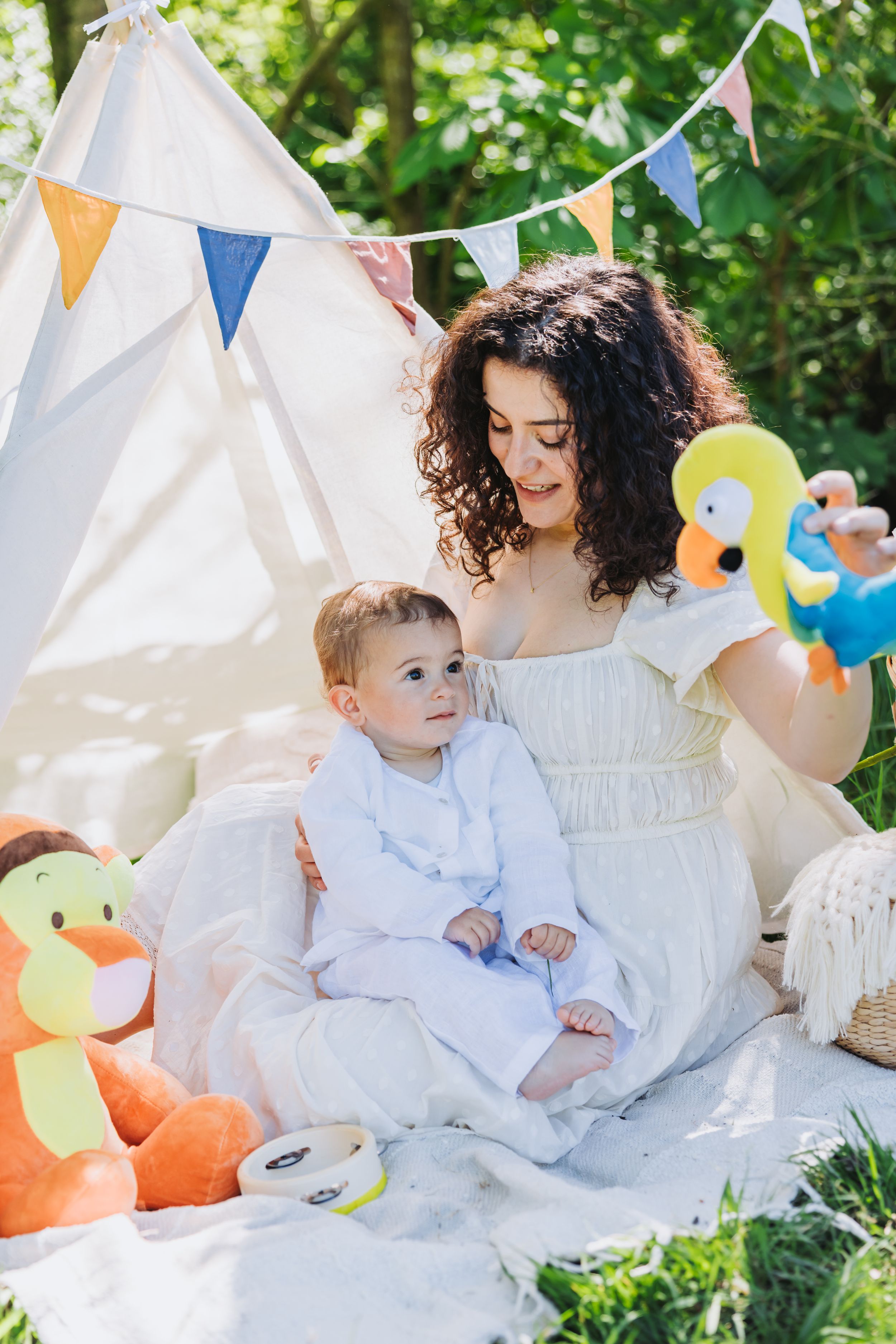 Candid lifestyle portrait of smiling mother and child among lush greenery with playful boho decor and plush toys