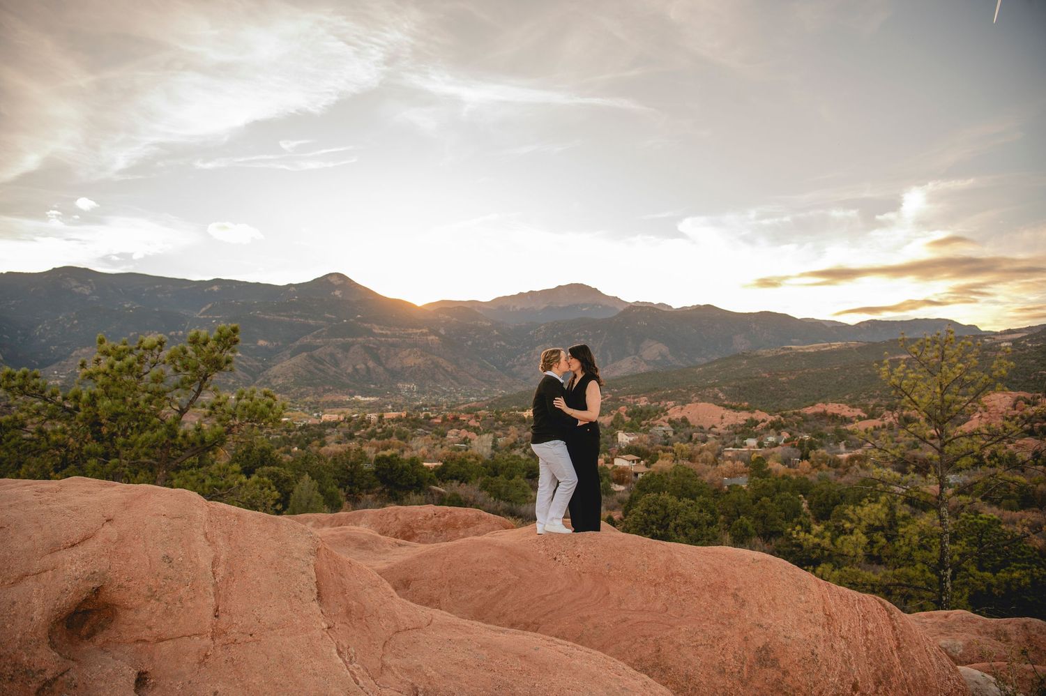 Couple embracing on red rocks at sunset with mountain landscape backdrop at Garden of the Gods.