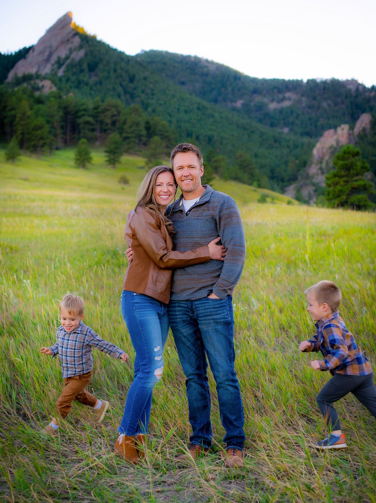 Family portrait in mountain meadow with children playing in background.