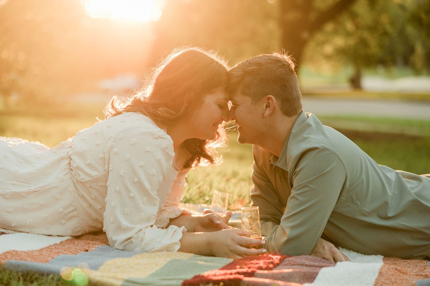 A romantic couple shares tender moments at sunset in a park setting during their engagement photo session.