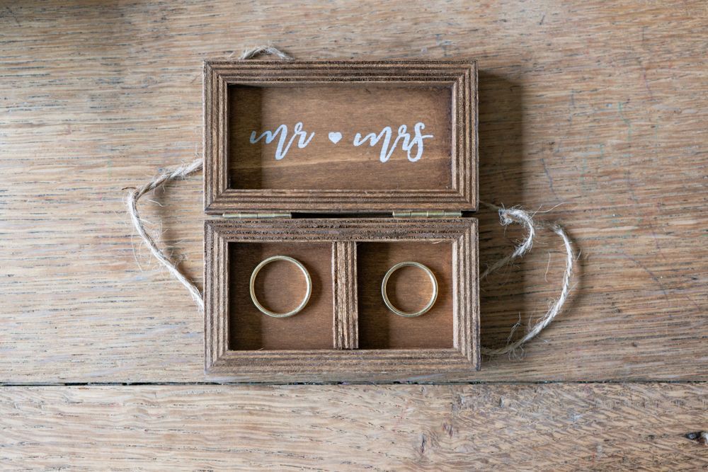 Rustic wooden Mr. and Mrs. ring box with two gold wedding bands on a wood surface.