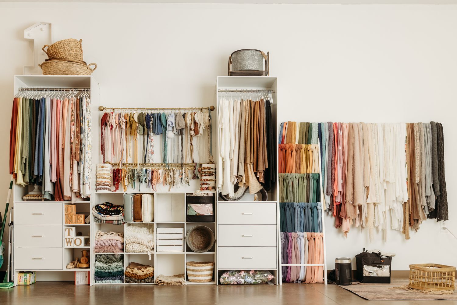 Organized boutique closet with colorful hanging clothes, white shelving units, and fabric swatches displayed on a wall.