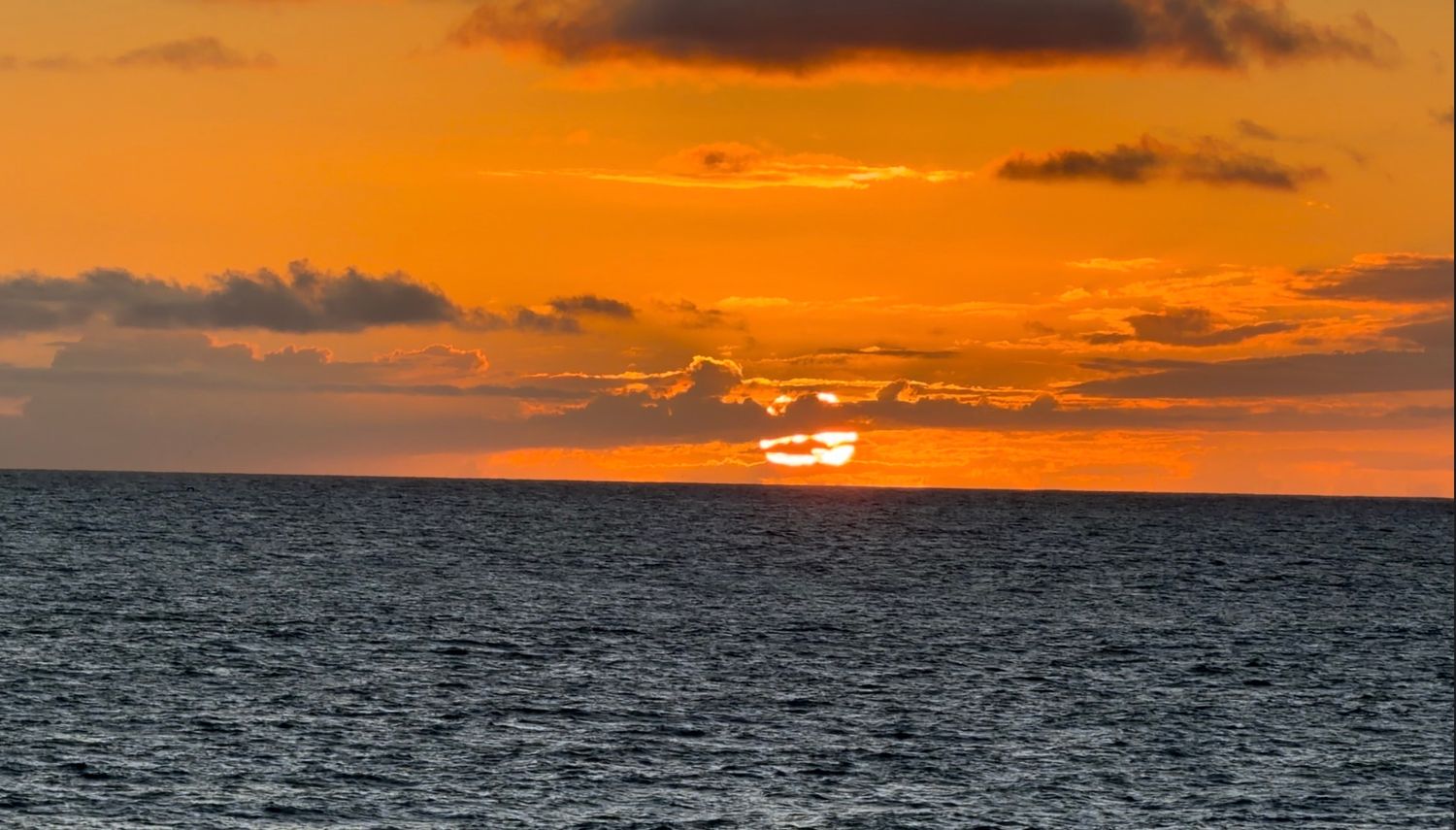 Vivid orange sunset over calm ocean waters with dramatic clouds on the horizon.