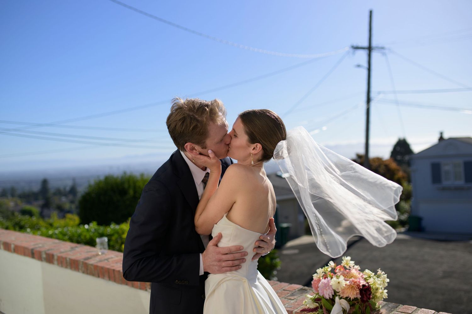 A bride and groom kiss with views of the San Francisco Bay behind them.