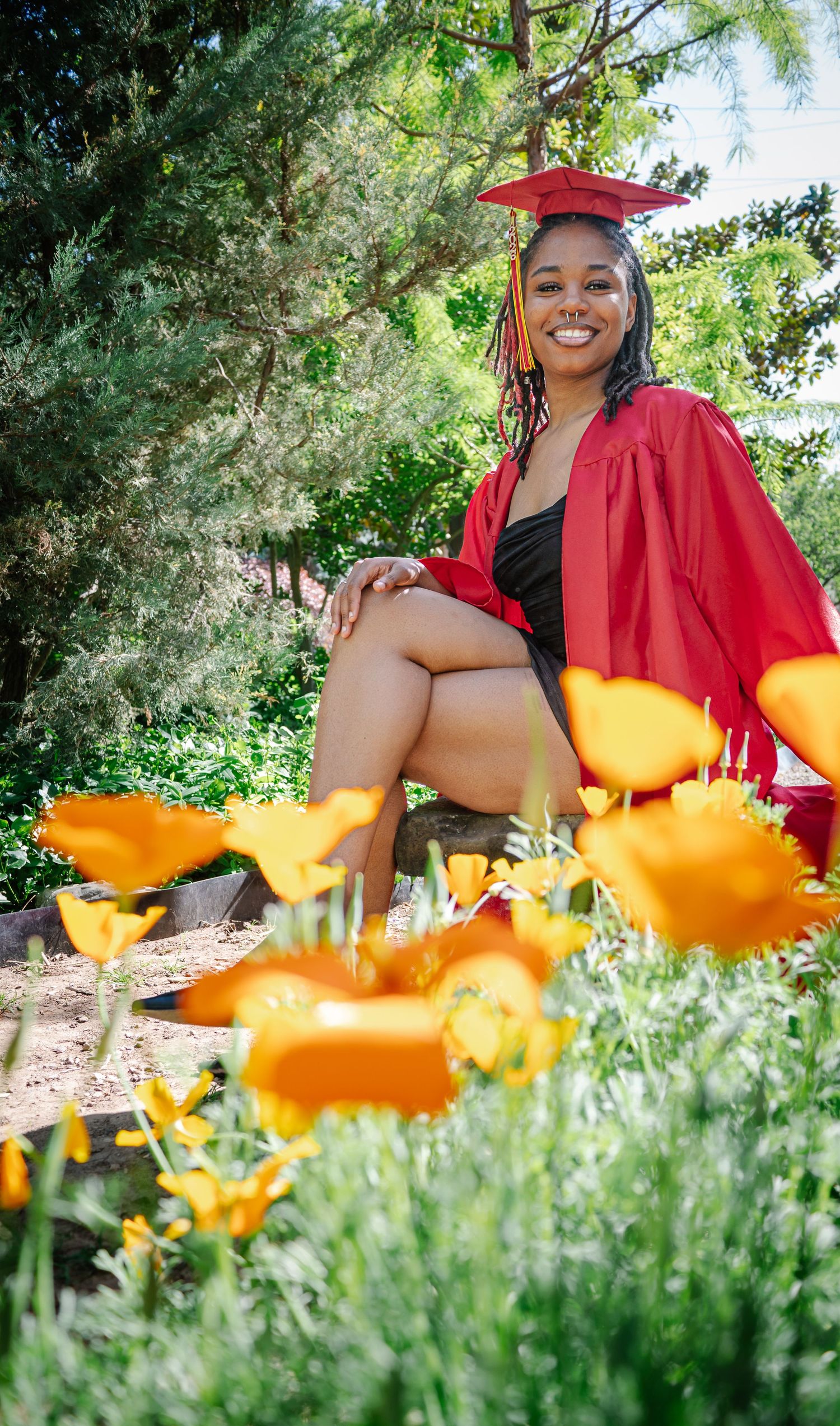 Class of 2026 senior sitting in red graduation gown during garden senior photo session
