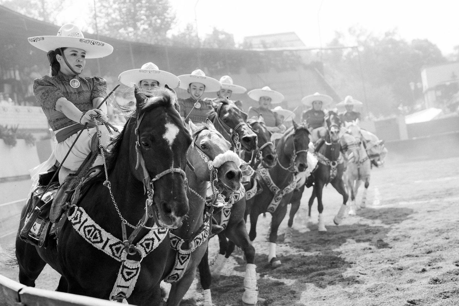 Mexican charreada equestrian show with riders in traditional costumes performing in a sandy arena.