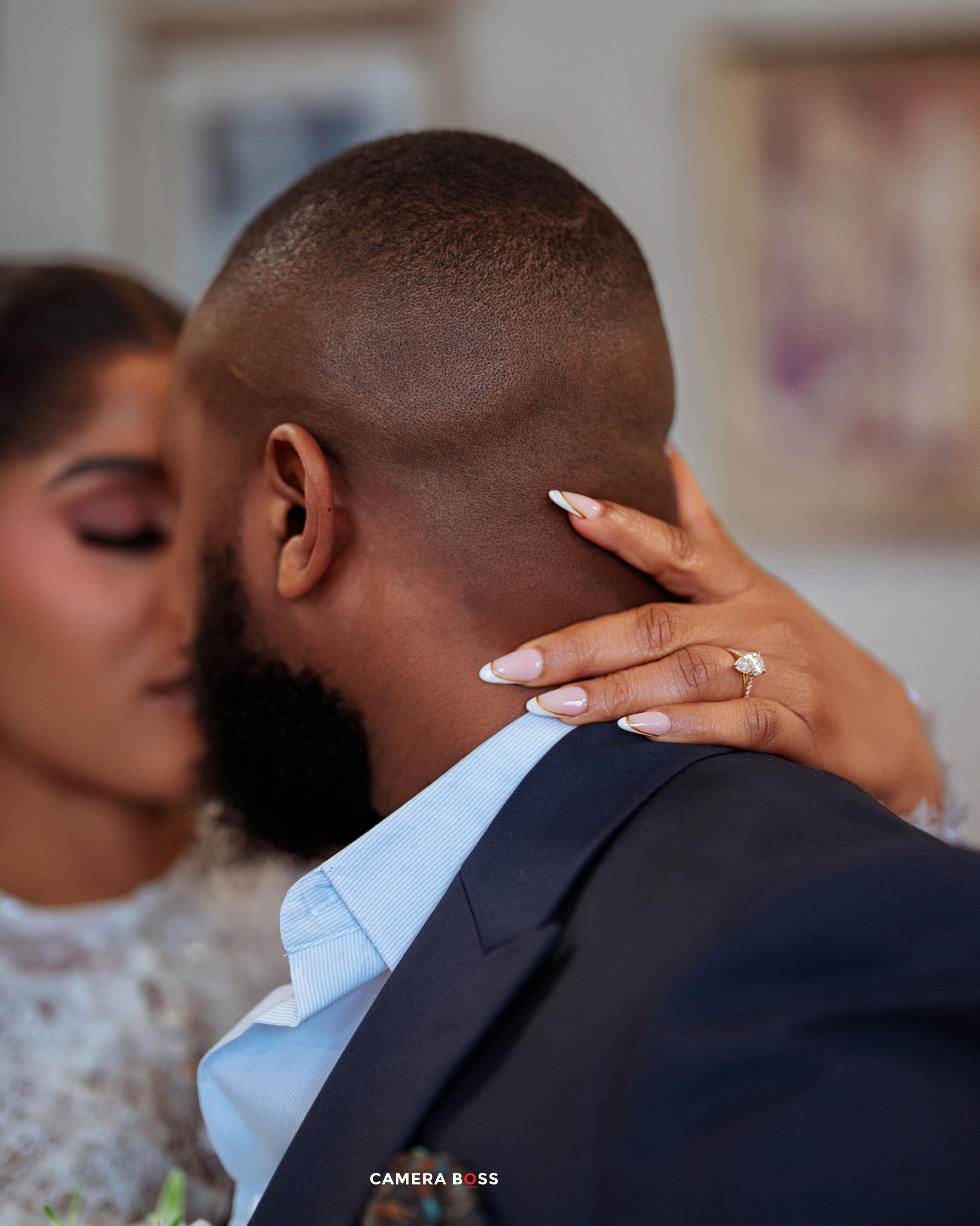 Couple sharing a romantic embrace, woman with French manicure and engagement ring gently holding mans neck during wedding.