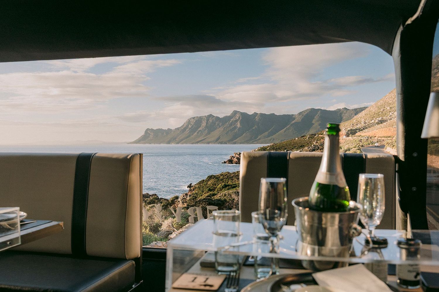 Champagne bottle in ice bucket on elegant table with stunning coastal mountain views from a luxury yacht.