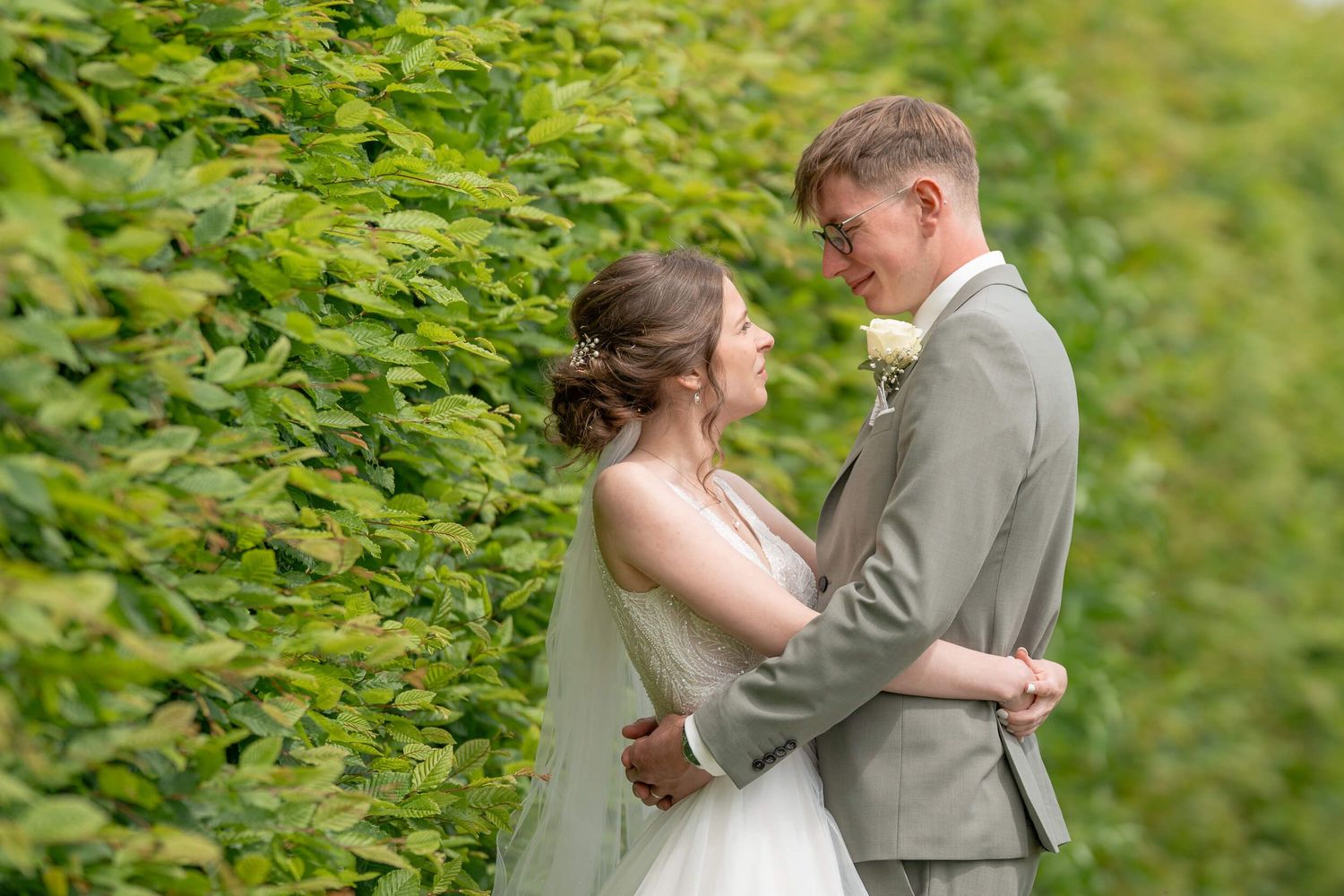 A couple shares a tender moment on their wedding day against a lush green garden backdrop.