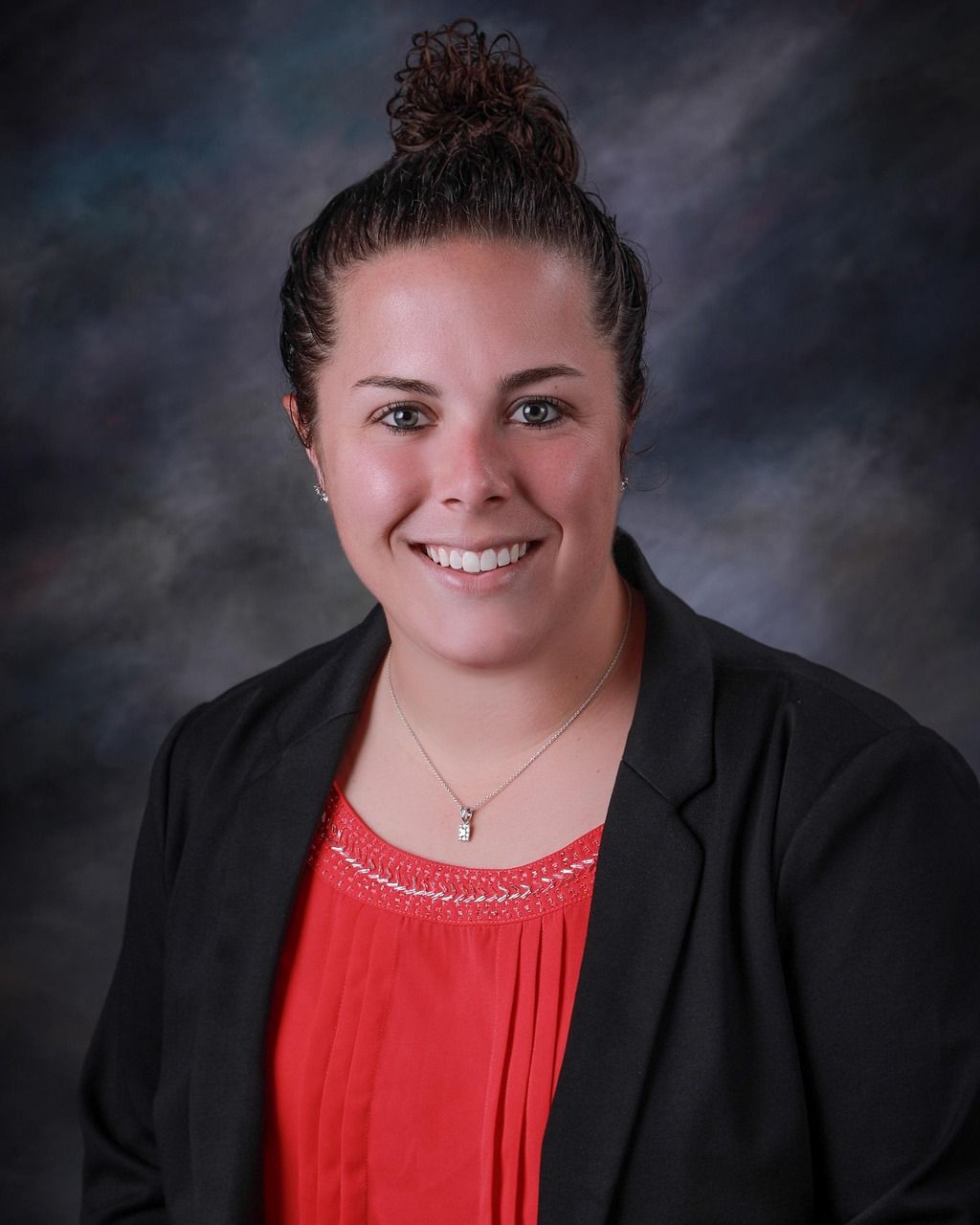 Professional headshot of someone wearing a black blazer and red top against a dark studio background.