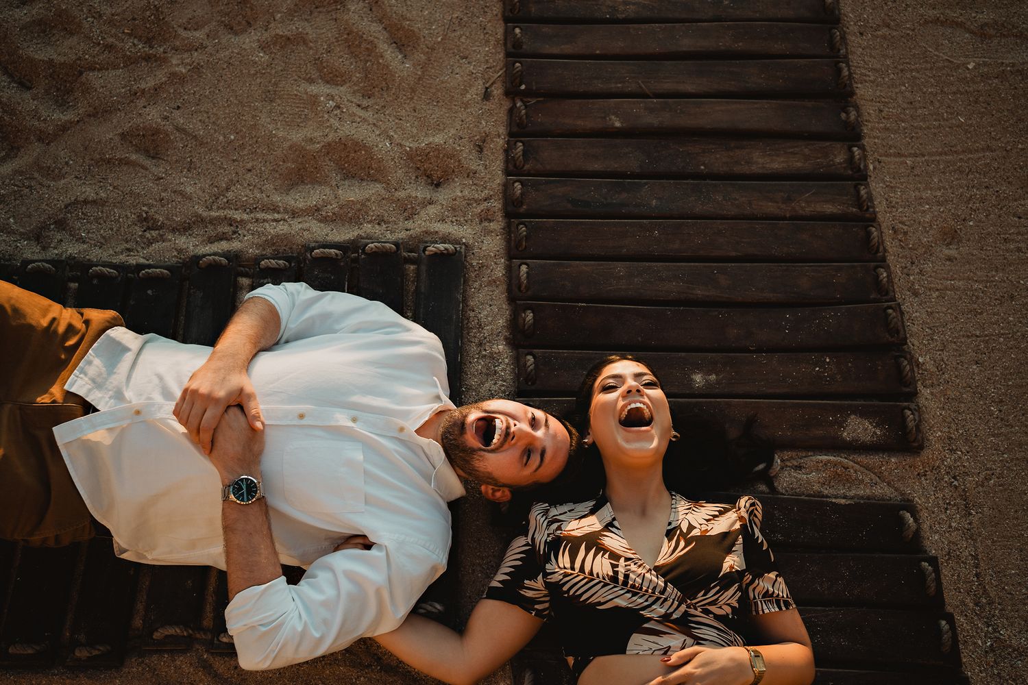 The couple lying on wooden planks, shouting and having fun, capturing their playful connection in Mazatlán