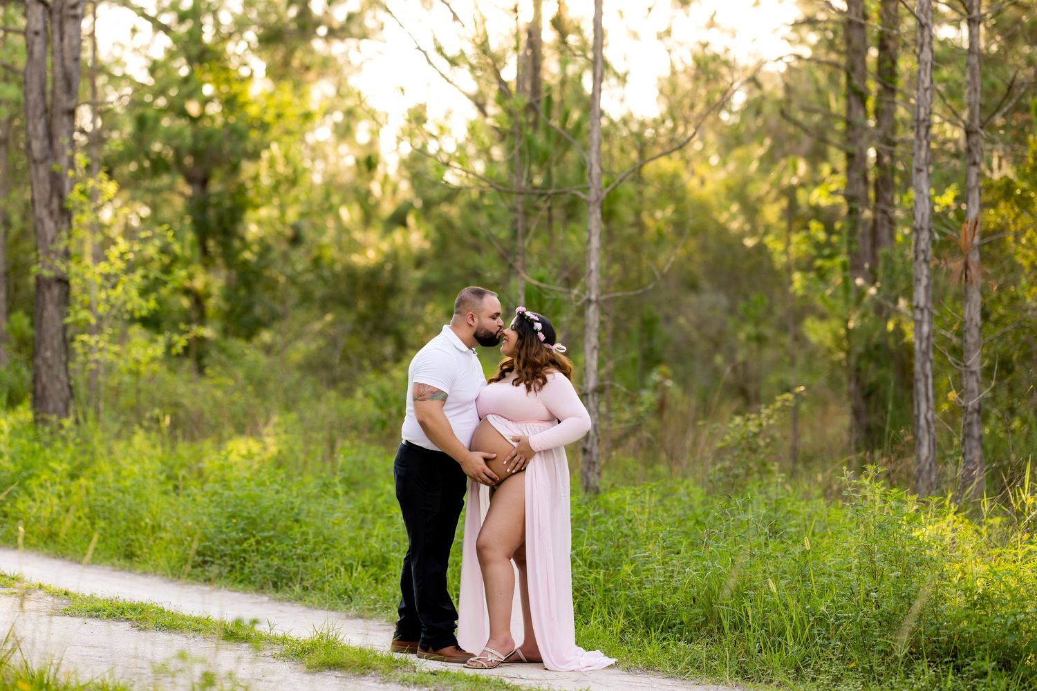 Romantic maternity photoshoot on wooded path during golden hour.