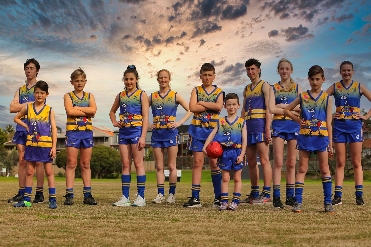 Youth sports team in blue and yellow uniforms posing together at sunset on a field.