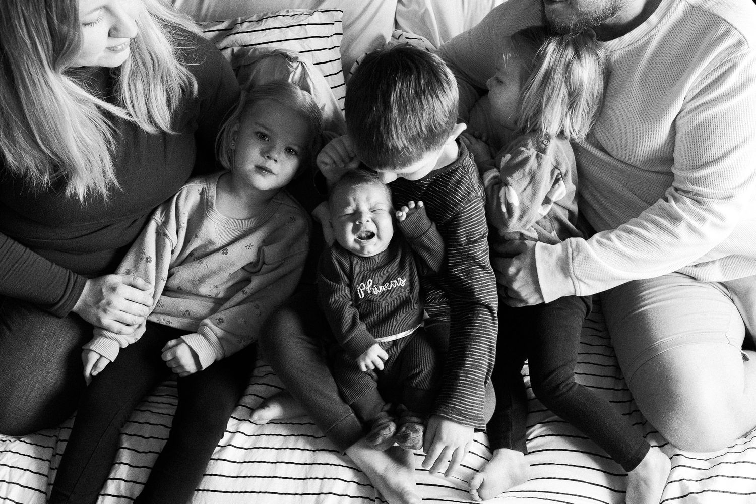 A black and white candid family portrait shows children and adults sitting together on a textured surface.