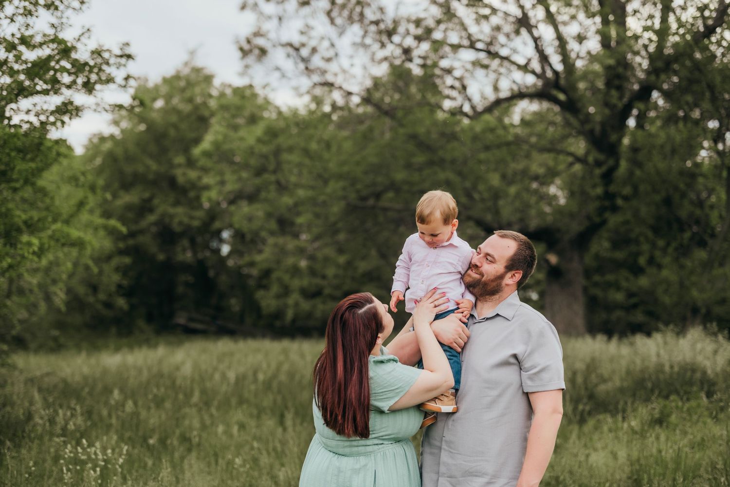 Family embraces in an outdoor summer photo session among lush green trees.