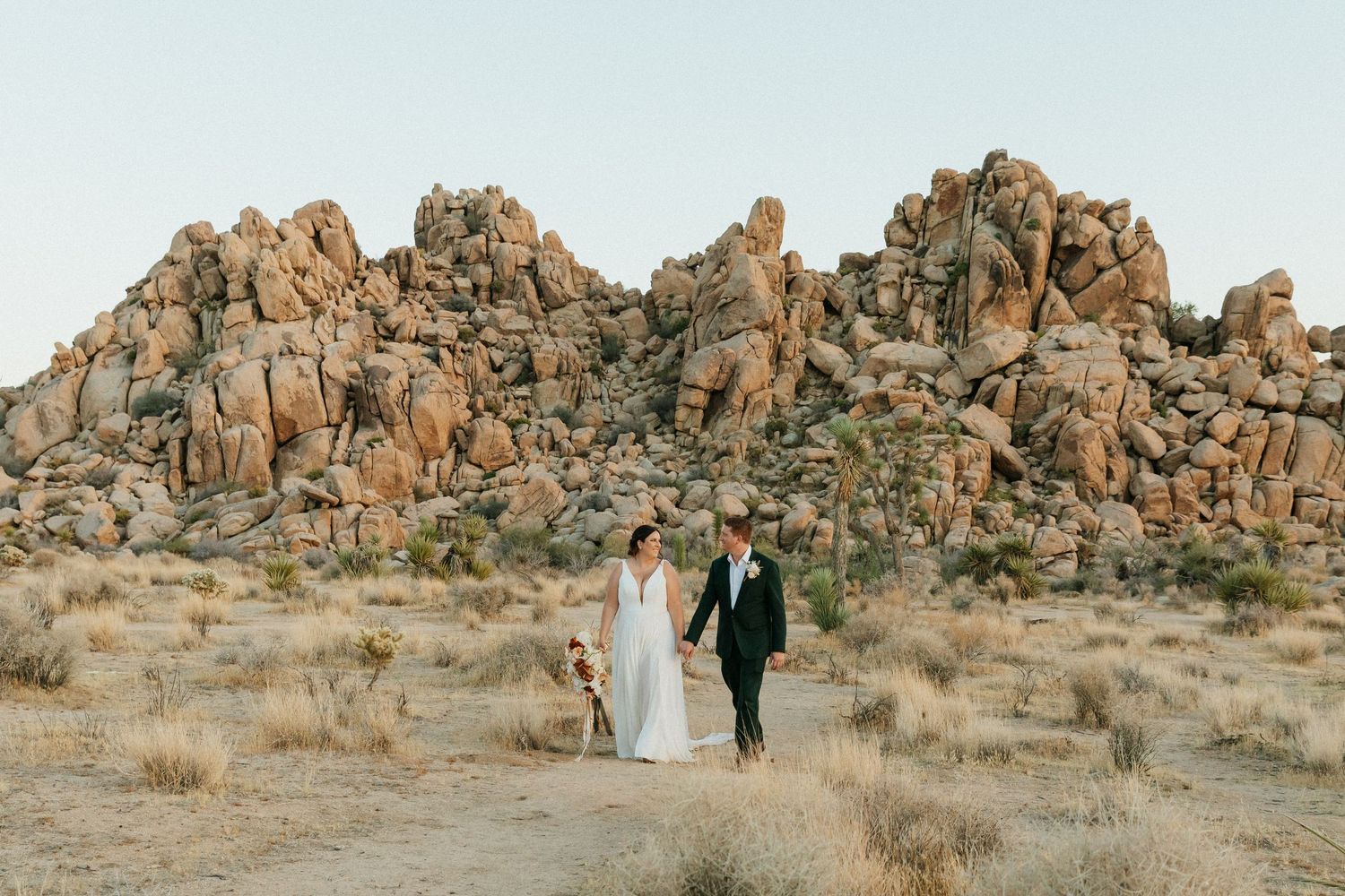 Bride and groom pose on Joshua Tree rocks during golden hour sunset