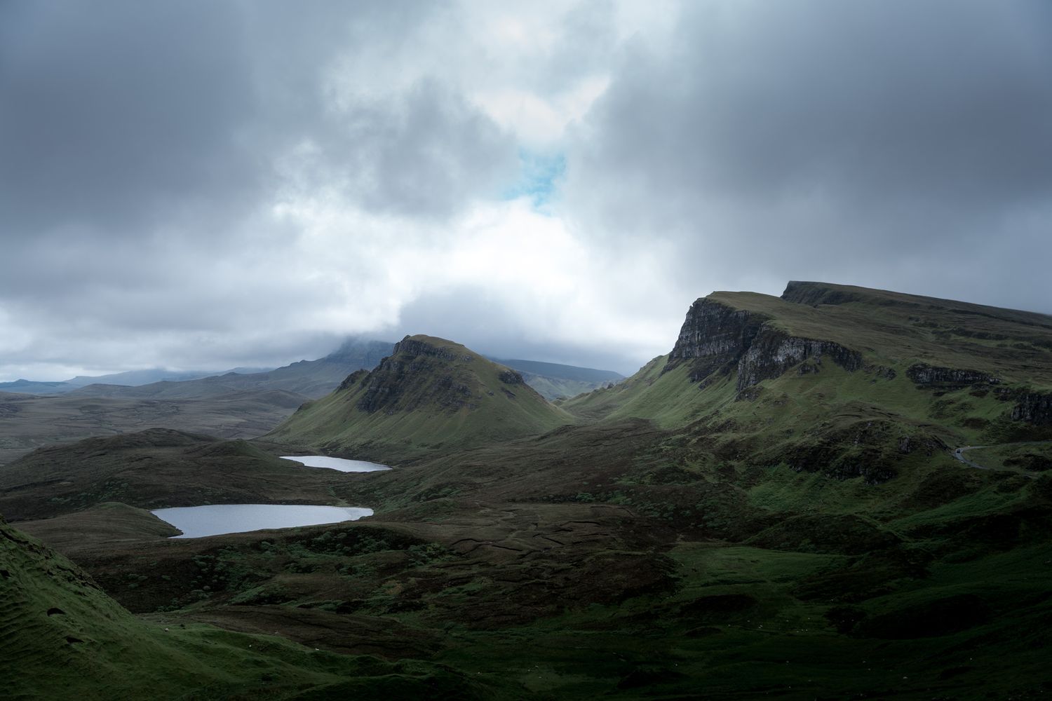 Dramatic panoramic landscape of misty green hills and mountains in Scotland with moody overcast skies.