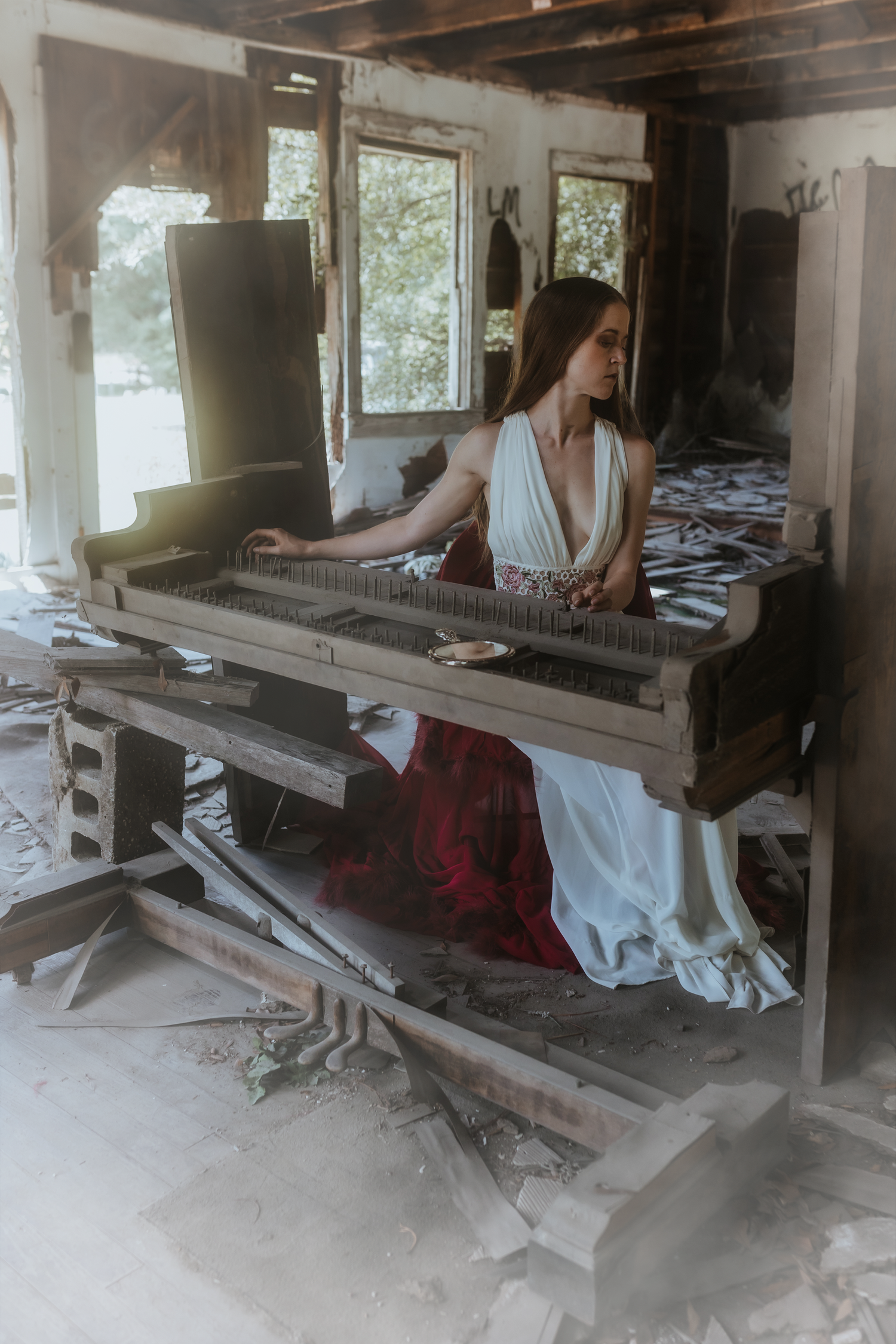 A woman in an abandoned church is seated at the remains of a piano