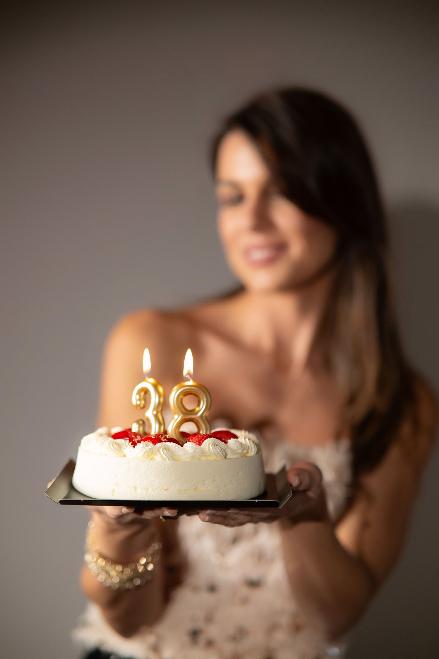 A birthday cake with golden number candles and raspberries is presented on a plate against a blurred background.