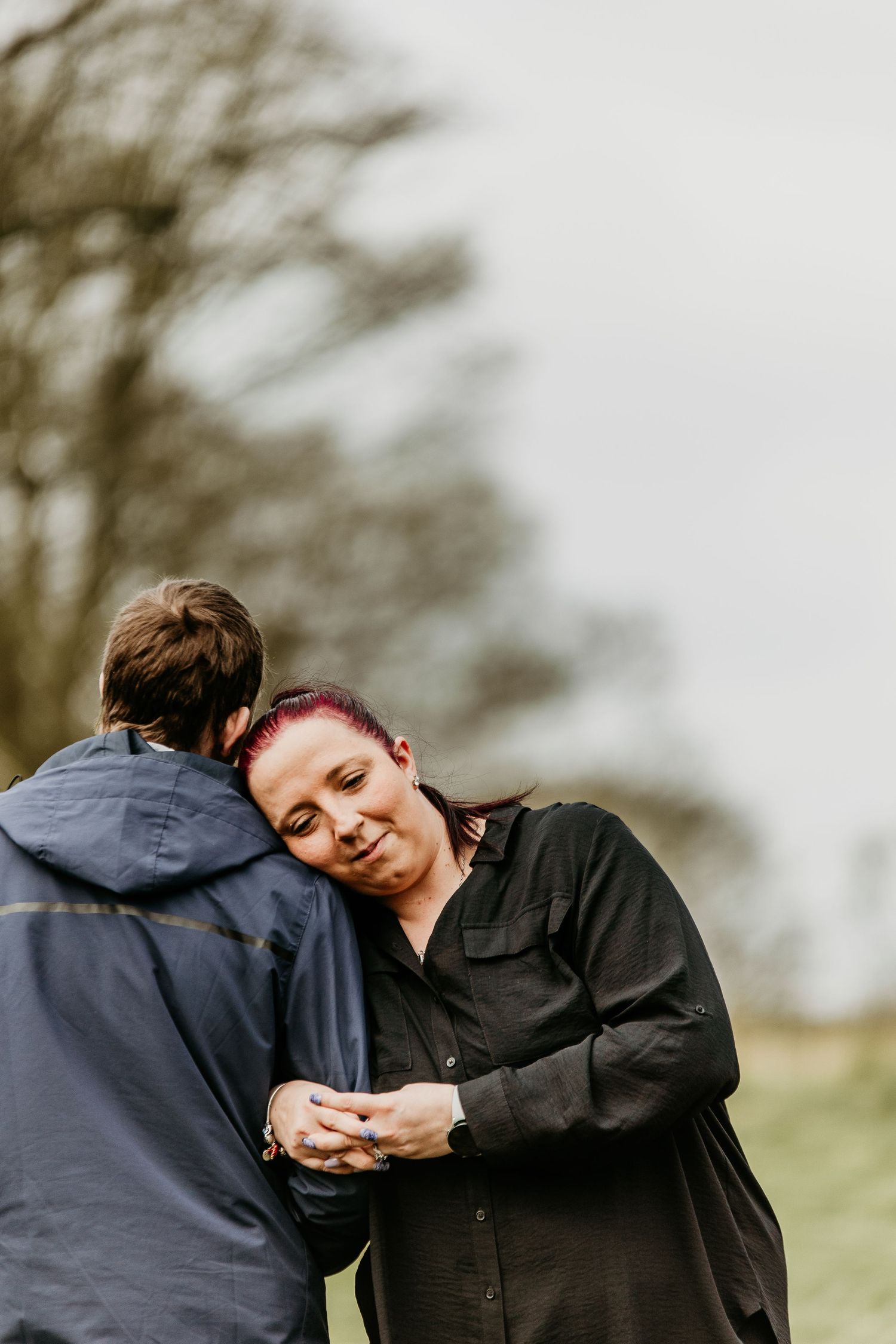 Couple shares an intimate moment outdoors while standing close together on a cloudy day.