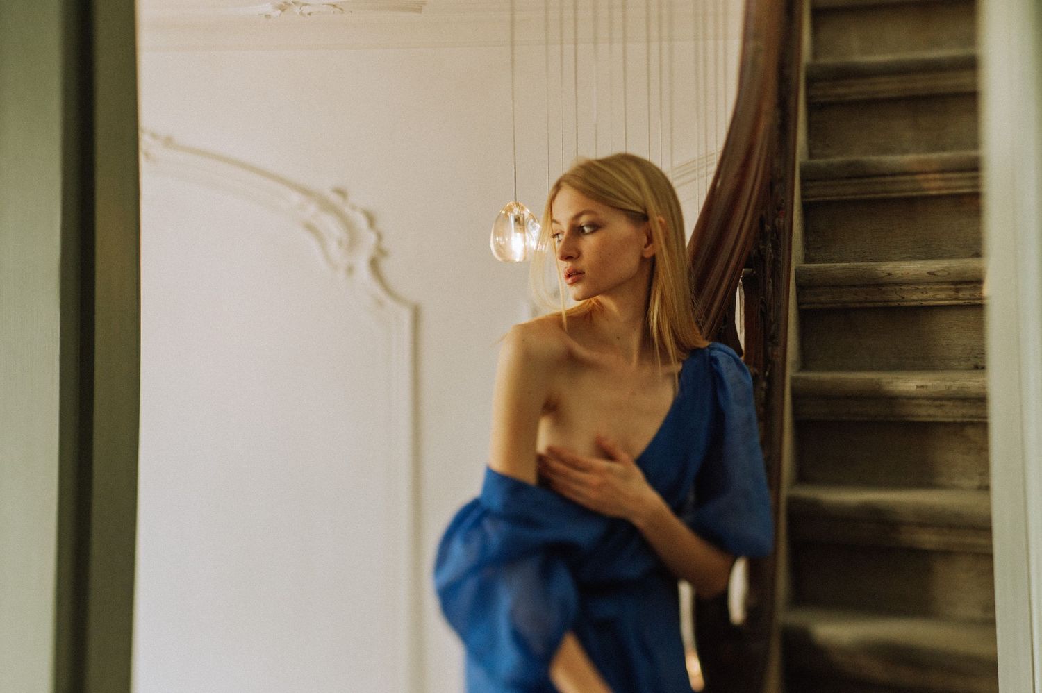 Artistic portrait near staircase with natural window lighting and dramatic shadows.