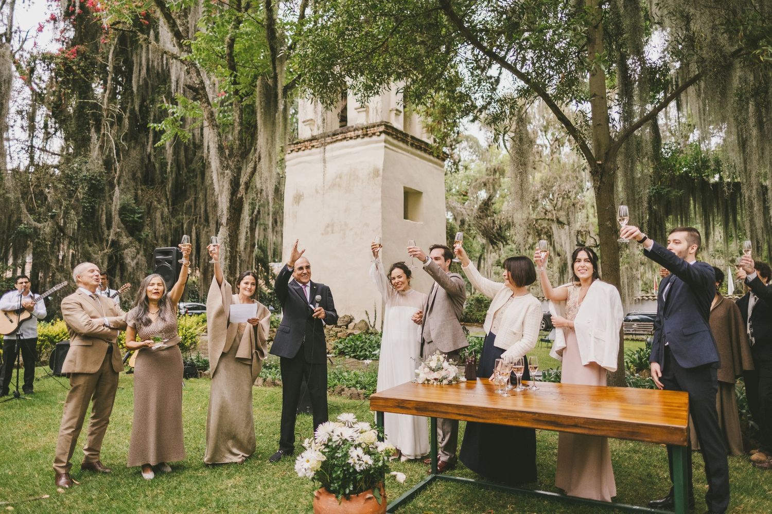 Outdoor wedding ceremony celebration with guests gathered around wooden table under Spanish moss draped trees.