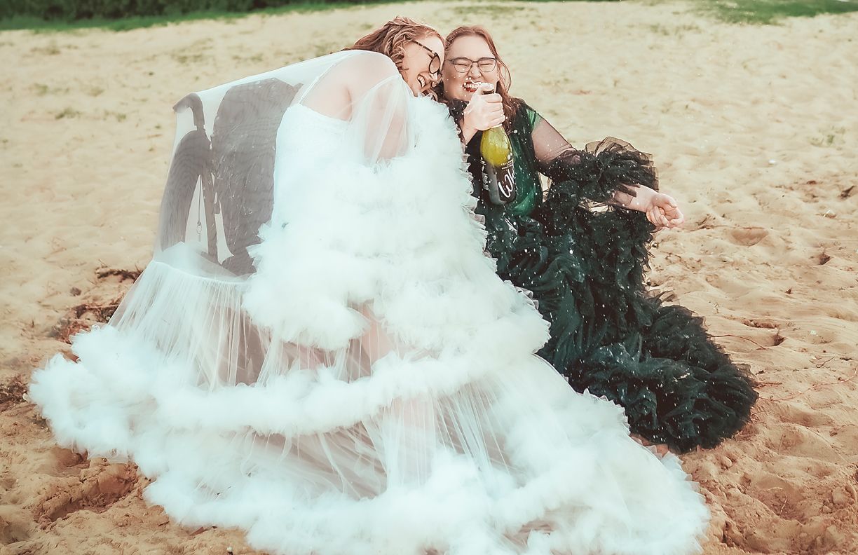 Two figures reclining on chairs outdoors with flowy contrasting black and white dresses on a sandy beach.