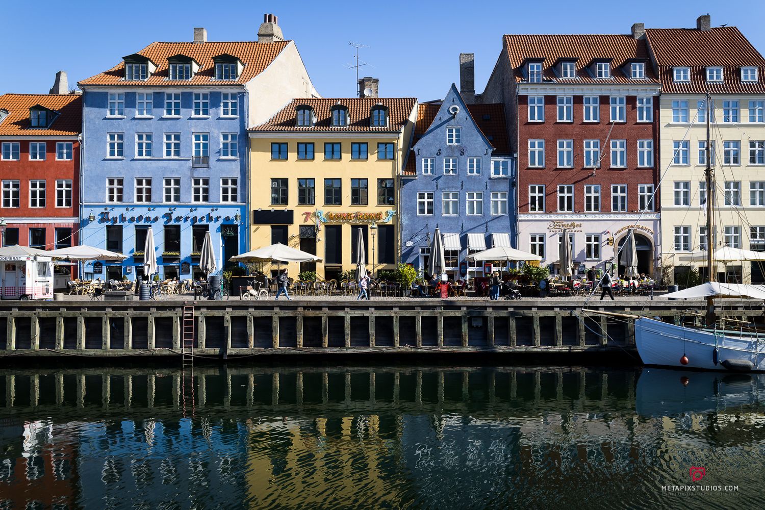 Colorful historic buildings with vibrant facades reflecting in the calm waters of Nyhavn canal in Copenhagen, Denmark.