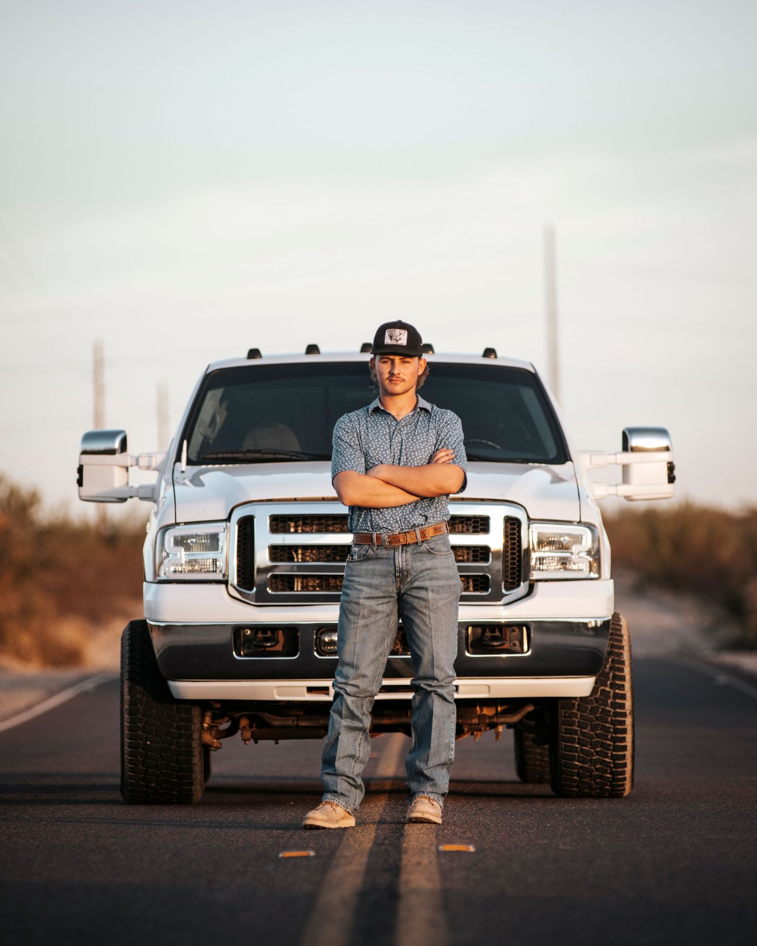 A lifted silver Ford pickup truck parked on a desert road with a saguaro cactus in the background at sunset.