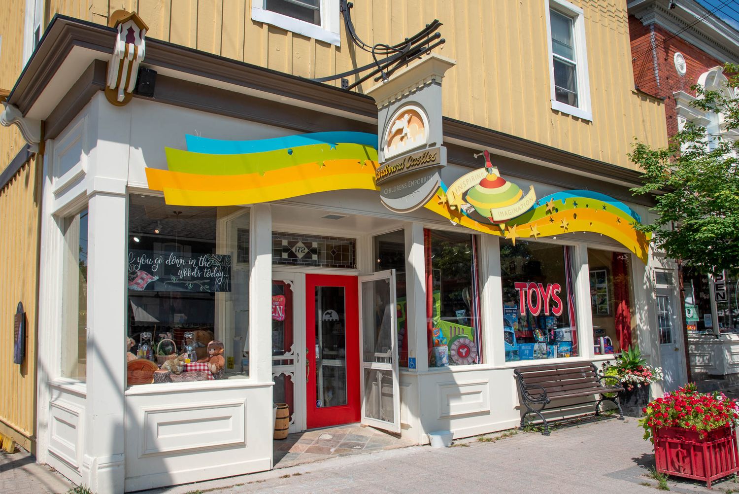 Charming yellow storefront of a dessert shop with colorful awnings and red flower boxes in a small town setting.