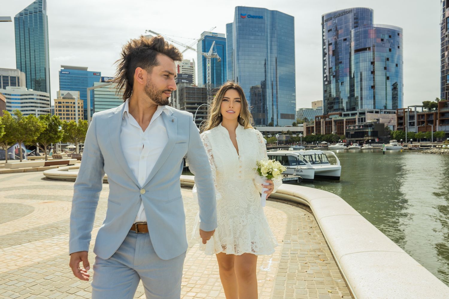 A couple walks along Elizabeth Quay with Perth's modern architecture in the background.