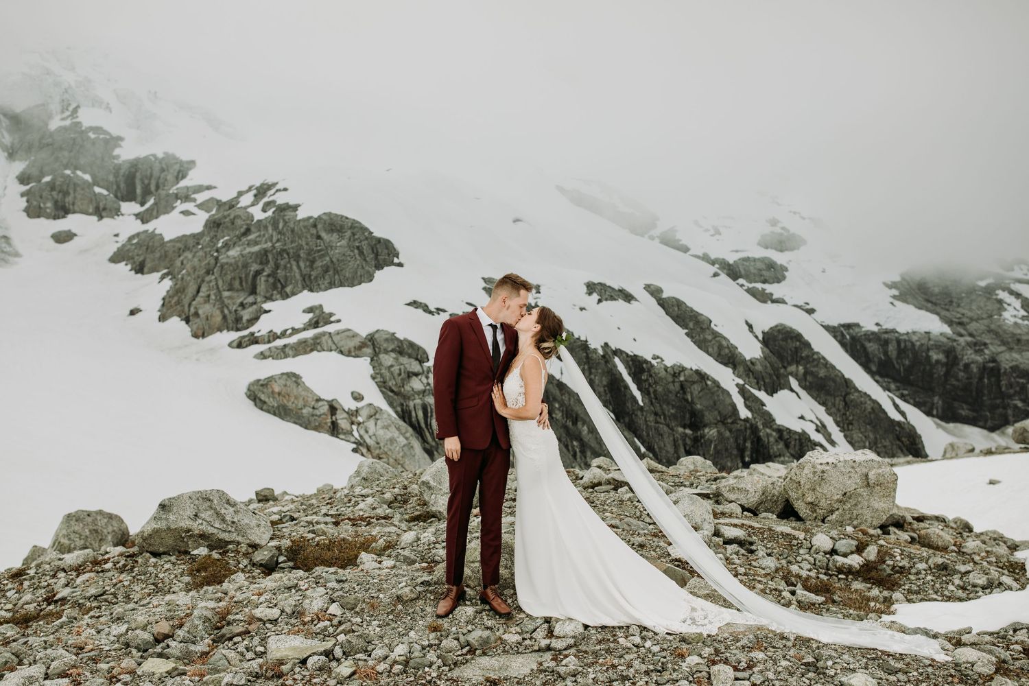 A dramatic wedding portrait against a snowy mountain backdrop with rocky terrain.