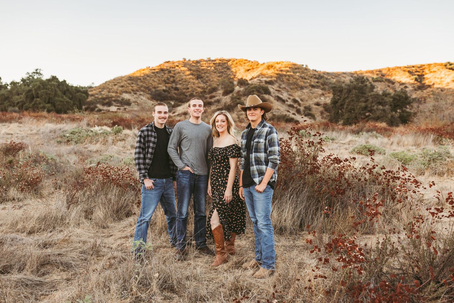Family wearing casual attire poses together in golden sunlit field during sunset photo session.