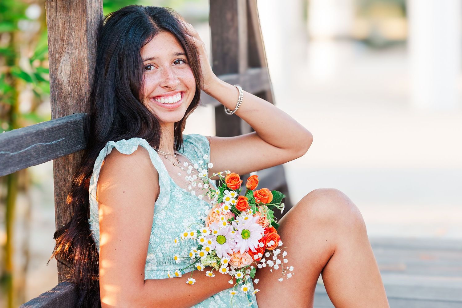 A person in a mint green dress poses with colorful wildflowers during a sunny outdoor photo session.