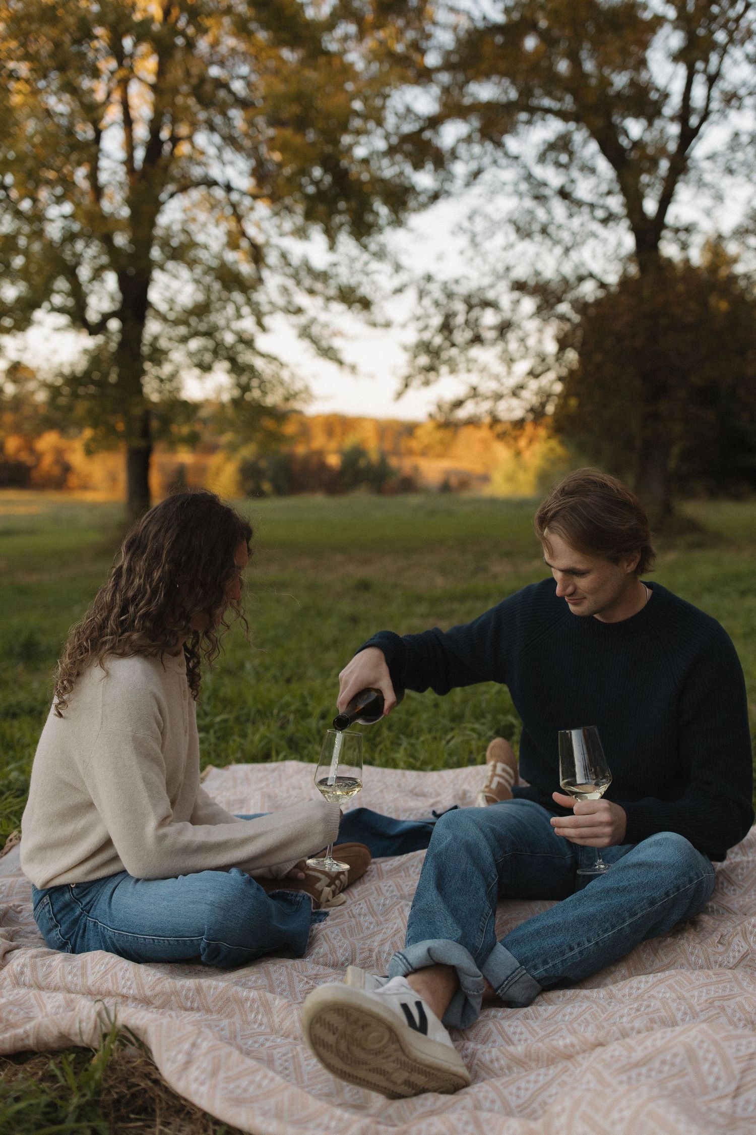 Couple lounging on a picnic blanket under autumn trees at sunset.