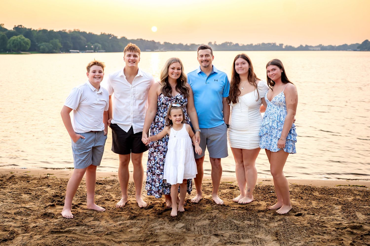 Family group poses for sunset beach portraits wearing coordinated blue and white outfits near the water.