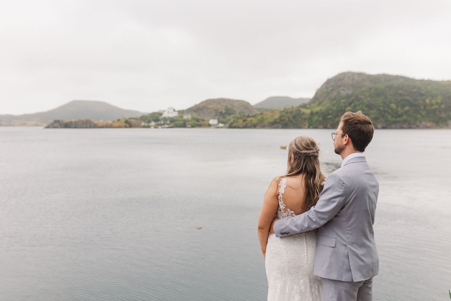 Two people share a romantic embrace while overlooking a scenic mountain lake on an overcast day.