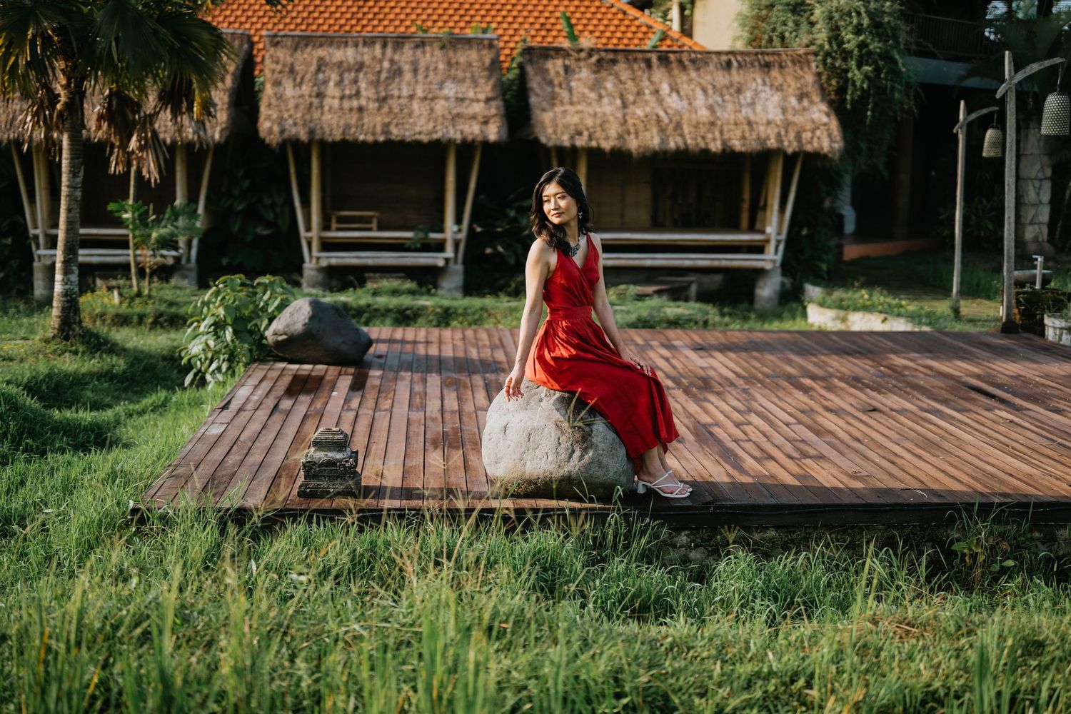 A peaceful garden setting with wooden decking and thatched roof structures surrounded by greenery.
