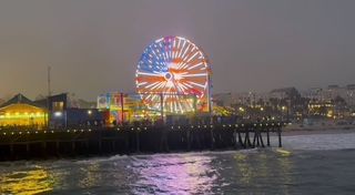 Illuminated Ferris wheel glowing red and blue at night along Santa Monica Pier.