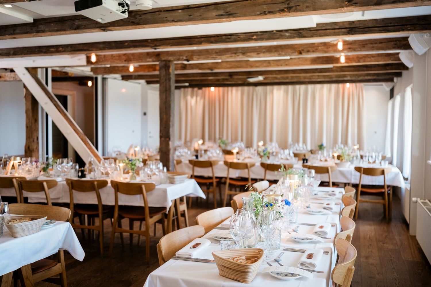 Rustic wedding reception venue with exposed wooden beams and elegant table settings under warm lighting.