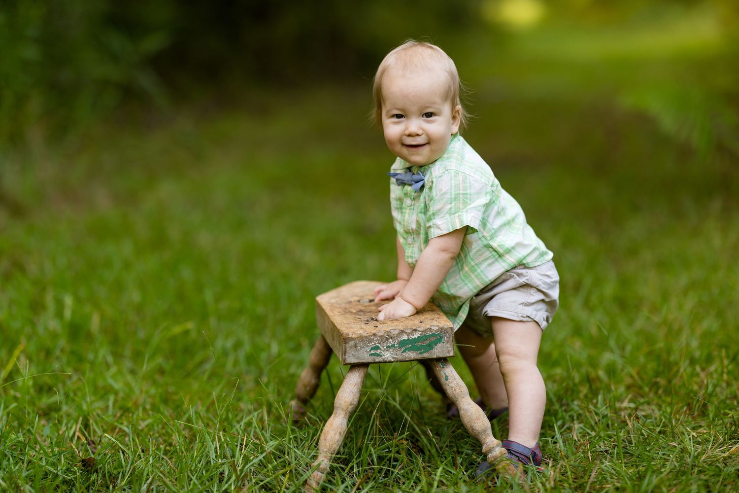 A baby wearing green and white crawls playfully on grass during a sunny outdoor photoshoot.