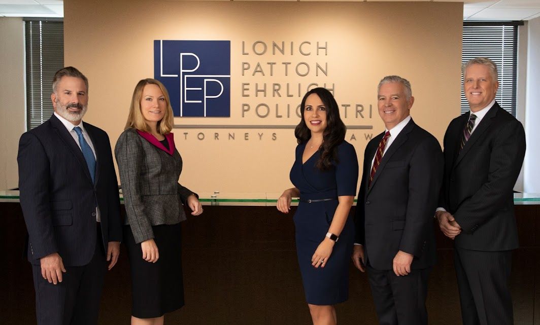 Group of business professionals posing in front of corporate logo wall display.