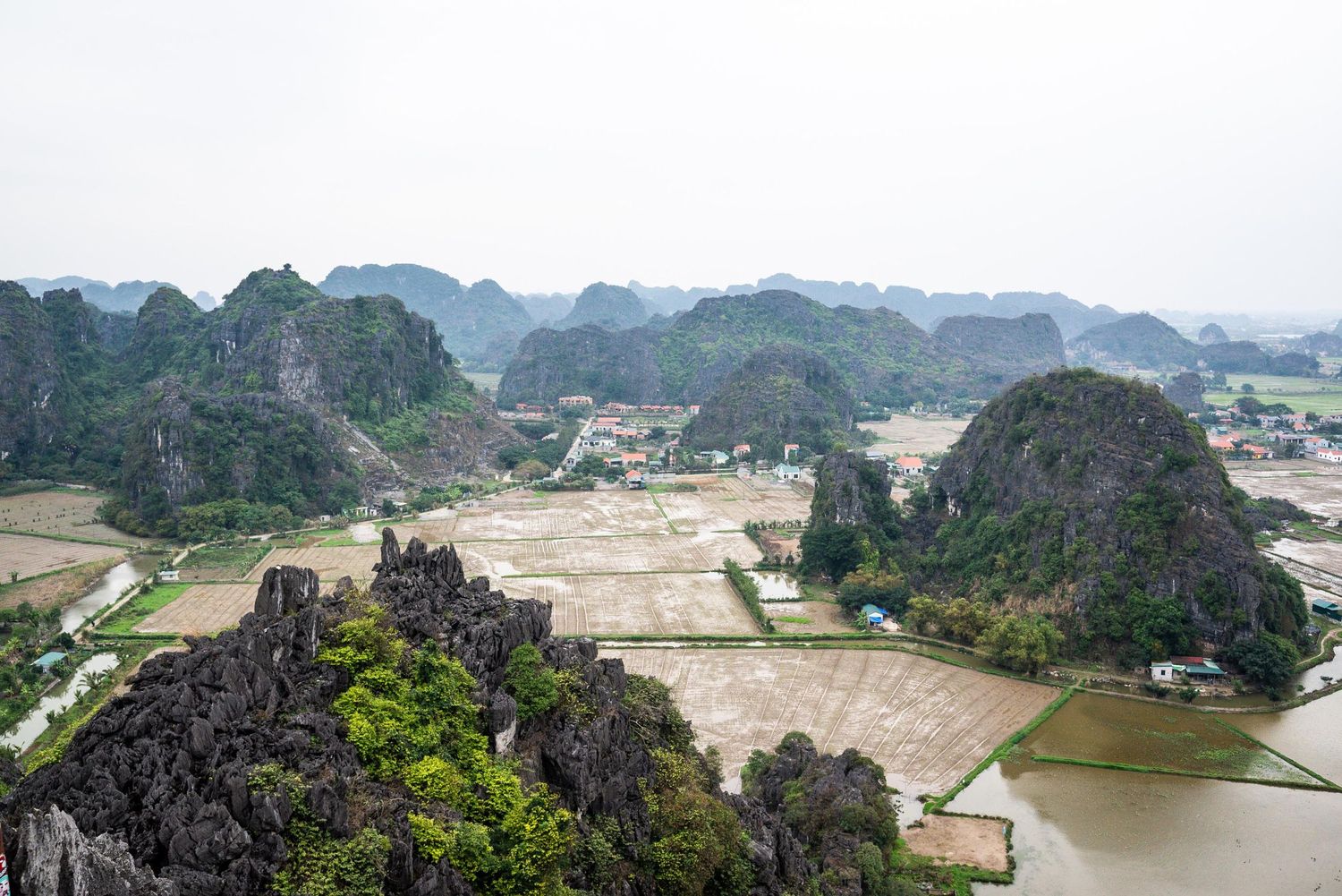 Aerial view of dramatic limestone karst mountains rising above rice paddies in Ninh Binh, Vietnam.