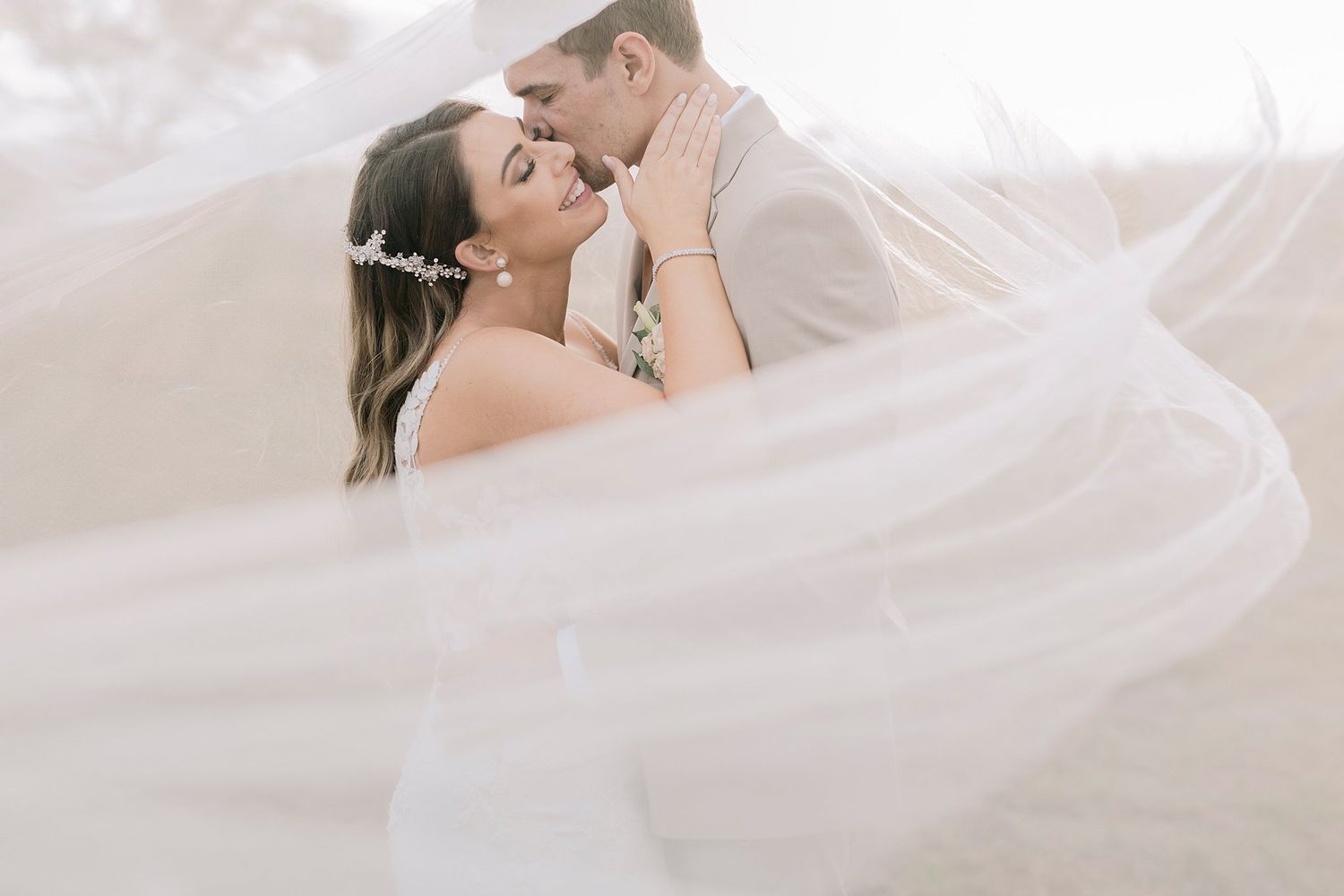 Bride and groom share a romantic moment wrapped in a flowing white veil on their wedding day.