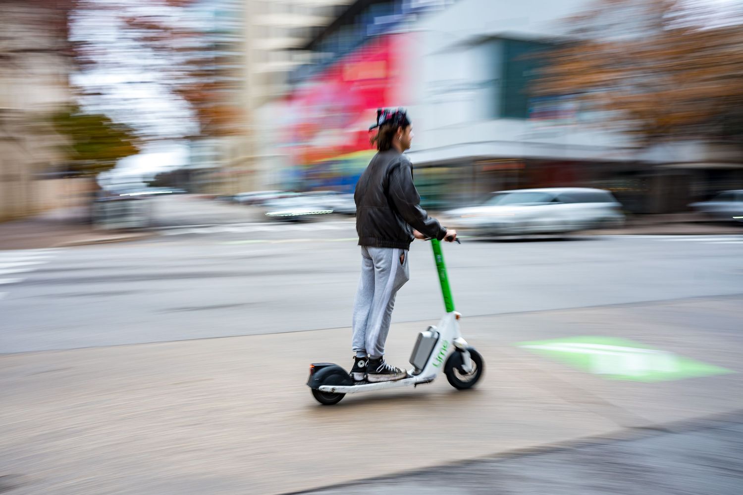 Person riding a Lime electric scooter through a city intersection with motion blur effect.