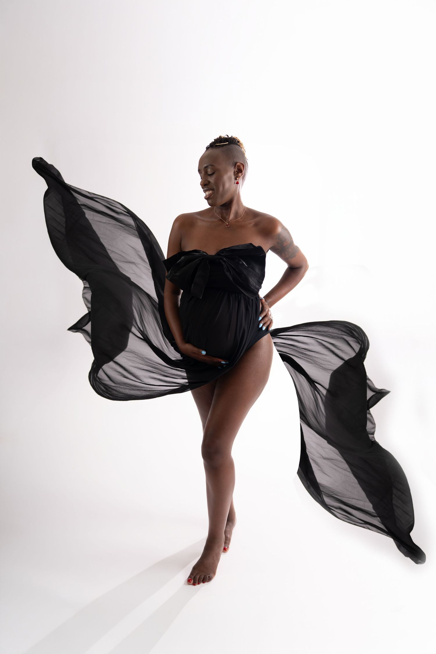 Artistic maternity photo with flowing black fabric against white background as figure poses gracefully in bodysuit.