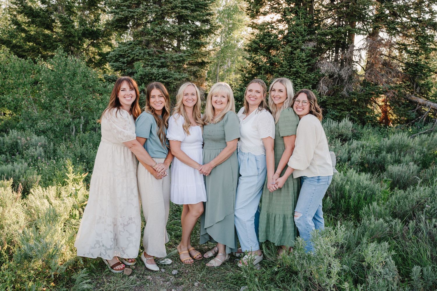 A group in coordinated light green and white outfits stands together outdoors among pine trees and greenery.