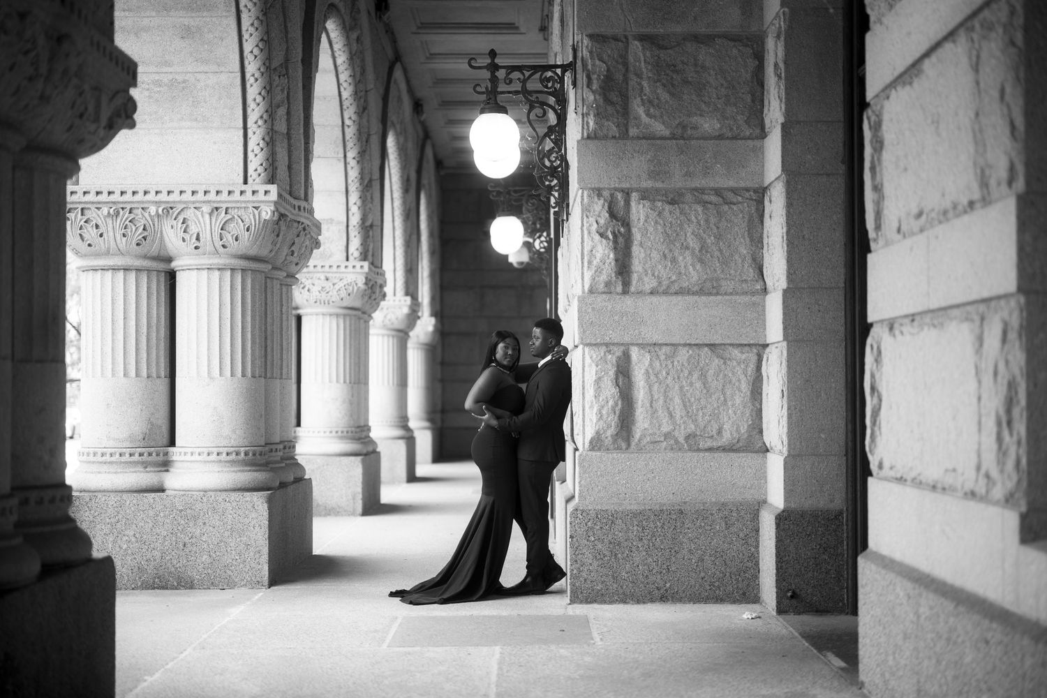 A couple dances in silhouette beneath ornate stone arches and columns in a black and white photograph.